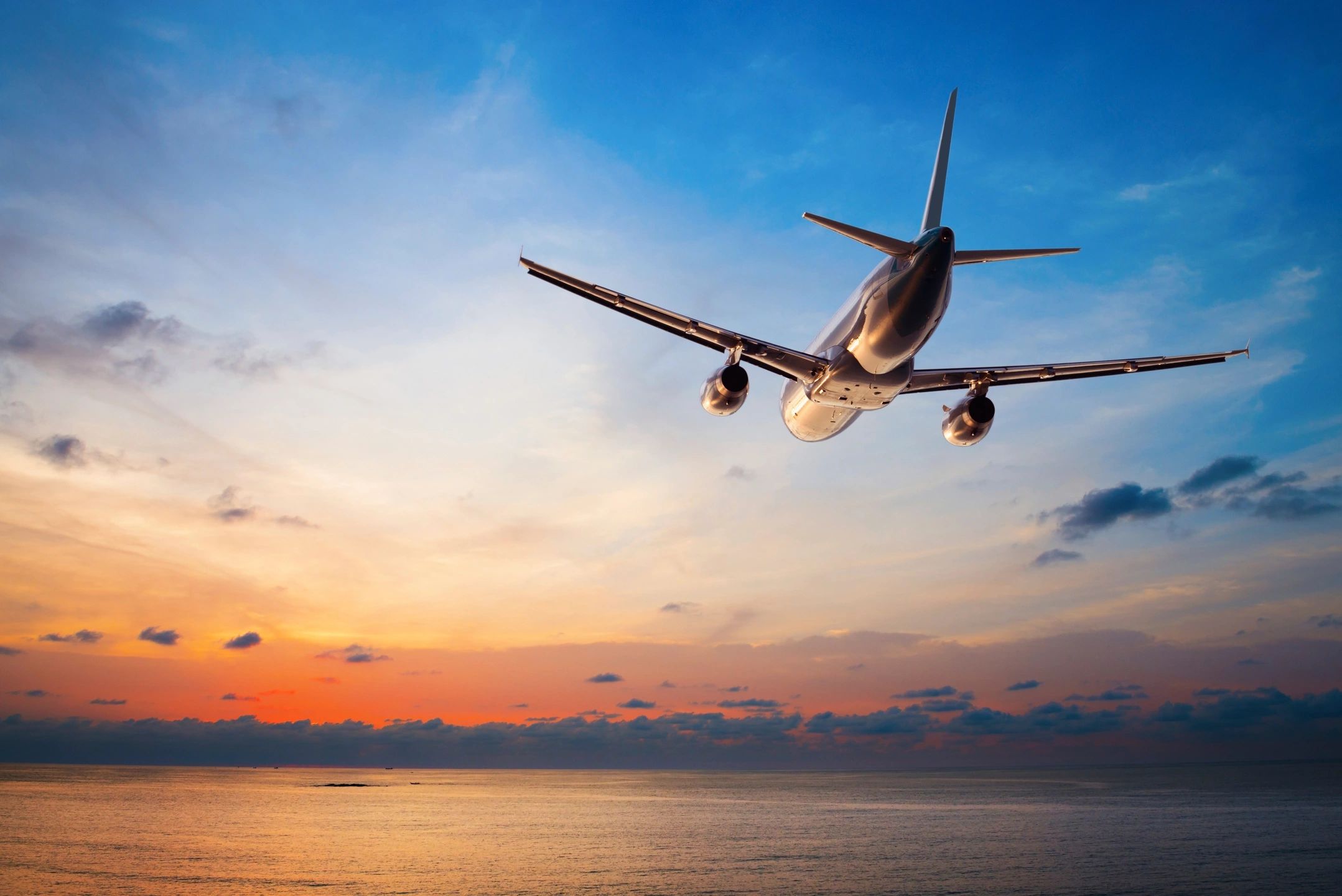 An airplane flying over the ocean towards the sunset